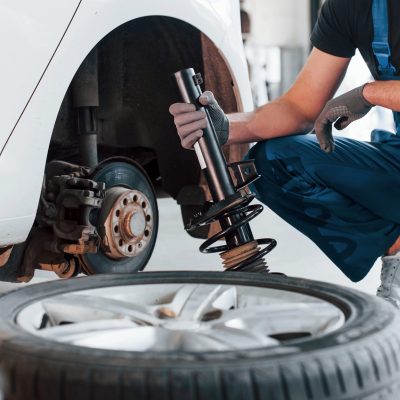 Man in work uniform repairs car indoors. Conception of automobile service.